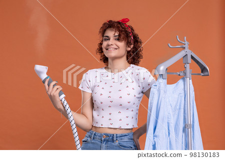 A woman with a smile on her face irons a man's shirt with a steamer. A woman with a smile on her face irons a man's shirt with a steamer. 98130183