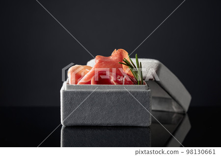 Prosciutto with rosemary in a gray gift box on a black background. 98130661