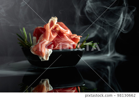 Prosciutto with rosemary on a black background. 98130662