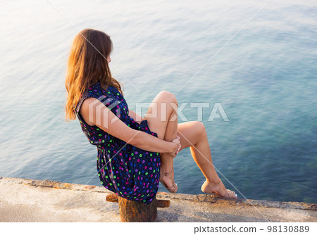 The girl in a beautiful dress is sitting on the pier. The girl in a beautiful dress is sitting on the pier. 98130889