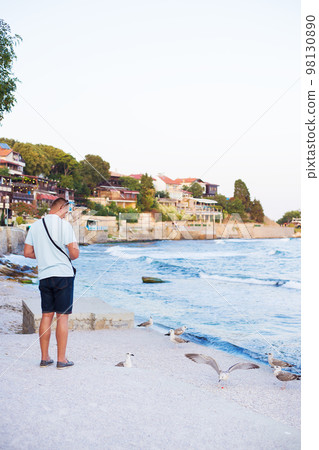 A young guy is feeding a flock of seagulls. Sun, summer, sea. A young guy is feeding a flock of seagulls. Sun, summer, sea. 98130890