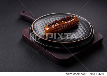 Delicious fresh eclair with chocolate cream on a black ceramic plate Delicious fresh eclair with chocolate cream on a black ceramic plate 98131691