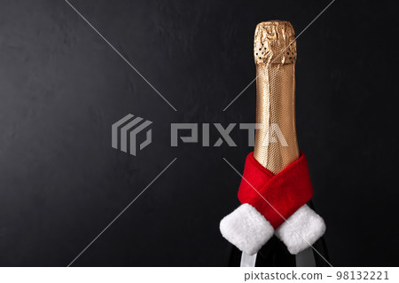 Champagne bottle wearing christmas hat and red knitting scarf on black background. New Year concept Champagne bottle wearing christmas hat and red knitting scarf on black background. New Year concept 98132221