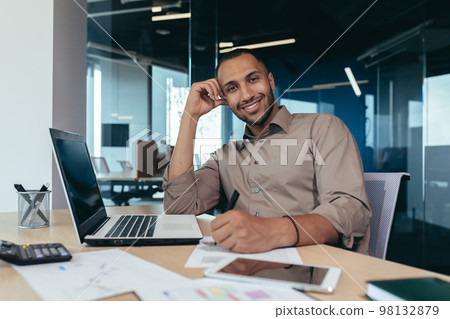 Portrait of successful hispanic businessman inside office, man with laptop working typing on keyboard smiling and looking at camera. 98132879