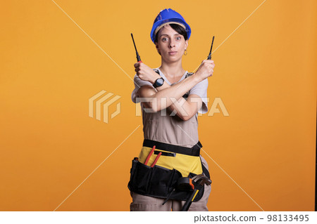Woman construction worker holding screwdrivers with both hands looking at camera in studio. Female building contractor doing stop sign and expressing refusal or rejection, x shape. 98133495