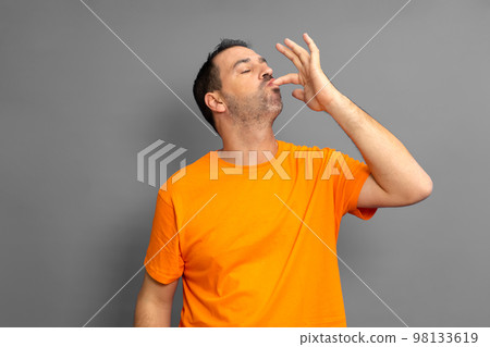 Happy man licking fingers isolated on trendy gray studio background. Beautiful male half-length portrait. Satisfied man. Human emotions, facial expression concept. Front view. 98133619