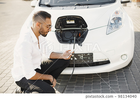 Young adult man charging his electric car in the city. Eco electric car concept. 98134040