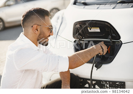 Young adult man charging his electric car in the city. Eco electric car concept. 98134042