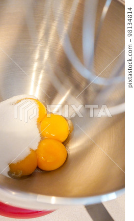Raw eggs in a metal bowl of standing mixer. Preparing egg yolk with sugar in kitchen mixer. 98134814