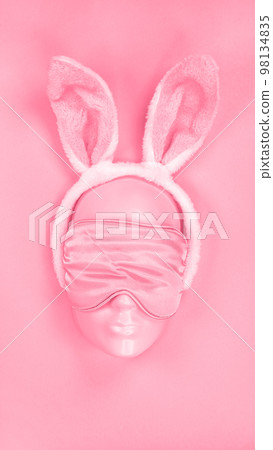 Pink sleeping eye mask on mannequin face with fluffy Easter bunny ears. Image is toned in Viva Magenta color of year 2023. sleeping disorder. Holidays, Head accessory. Plastic face. 98134835