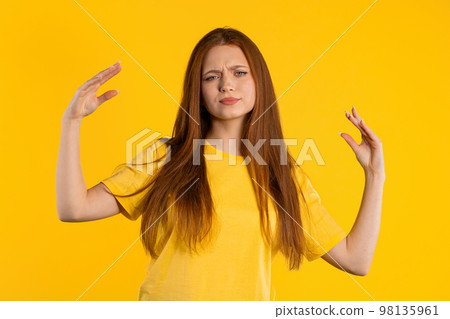 Irritated ginger woman showing bla-bla-bla gesture with hands, rolling eyes on yellow background 98135961