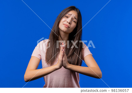 Young woman praying, begs to apologize her, she is guilty. Blue background. Hopeful prayer girl Young woman praying, begs to apologize her, she is guilty. Blue background. Hopeful prayer girl 98136057