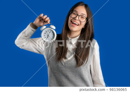 Happy student girl with alarm clock on blue background. Early morning, correct day routine, living Happy student girl with alarm clock on blue background. Early morning, correct day routine, living 98136065