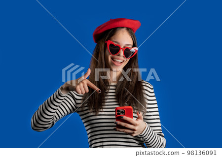 Smiling teenager girl pointing to smartphone, she advise mobile app, mobile operator. Young woman on 98136091