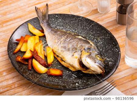 Grilled gilthead bream with side dish of baked potato Grilled gilthead bream with side dish of baked potato 98136596
