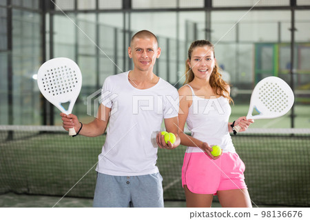 Couple of cheerful young paddle tennis players standing on indoor court 98136676