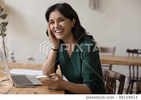 Happy freelance worker woman holding smartphone, sitting at work table Happy freelance worker woman holding smartphone, sitting at work table 98139813