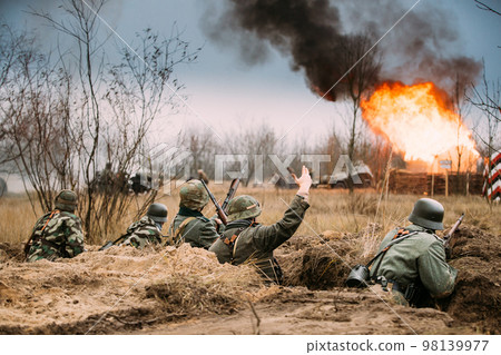 Defensive Position. Re-enactors Armed Rifles And Dressed As World War Ii German Wehrmacht Infantry Soldiers Fighting Defensively In Trench. Building On Fire On Background 98139977