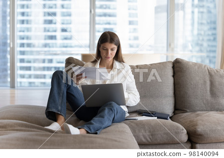 Busy woman sitting on sofa working or studying use laptop Busy woman sitting on sofa working or studying use laptop 98140094