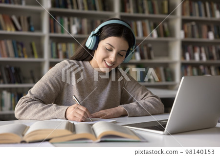Happy Latin student girl in wireless earphones studying in library Happy Latin student girl in wireless earphones studying in library 98140153