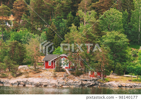 Sweden. Beautiful Red ASwedish Wooden Log Cabins Houses On Rocky Island Coast In Summer. Lake Or River Landscape 98140177