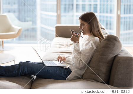 Woman use laptop holds cellphone blab on speakerphone with friend Woman use laptop holds cellphone blab on speakerphone with friend 98140253