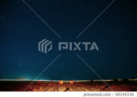 Agricultural Colorful Background Copy Space. Night Starry Sky Above Rural Landscape Field Meadow With Rolls Of Straw In Fields After Harvest. Glowing Stars And Sunset Lights Hay Bales After Harvest 98140336