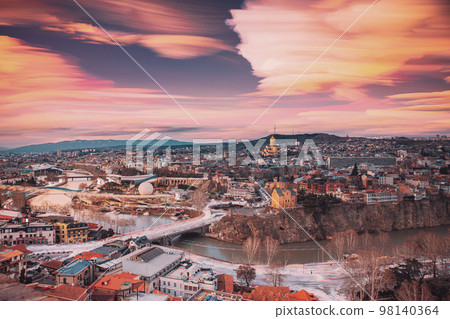 Tbilisi, Georgia. Amazing Dream Clouds Trails In Sky. Georgian Capital Skyline Cityscape. Fantasy City During Sunset And Night Illuminations. Unusual Cloudy Effects Sky. Top View Of Famous Landmarks 98140364