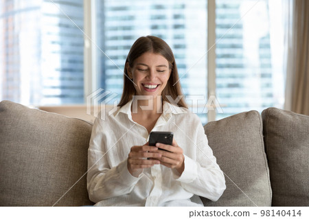 Young woman staring at smartphone screen, laughs, enjoy carefree leisure Young woman staring at smartphone screen, laughs, enjoy carefree leisure 98140414
