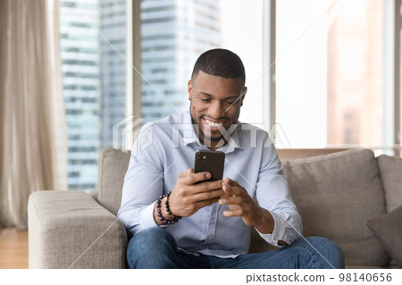 Handsome single African guy sit on sofa with cellphone Handsome single African guy sit on sofa with cellphone 98140656