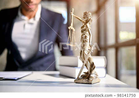 The Statue of Justice on a table over blurred background of professional male lawyer or attorney. The Statue of Justice on a table over blurred background of professional male lawyer or attorney. 98141750