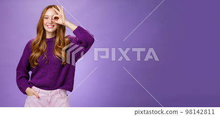 Optimistic girl looking into middle distance through okay gesture and smiling broadly with hopeful excited grin standing delighted over purple background in sweater and hand in pants Optimistic girl looking into middle distance through okay gesture and smiling broadly with hopeful excited grin standing delighted over purple background in sweater and hand in pants 98142811