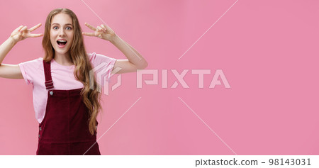 Girl staying positive lifting after falling. Charming carefree friendly-looking young woman with small scar on arm and tattoo showing peace gestures, open mouth and looking at camera over pink wall Girl staying positive lifting after falling. Charming carefree friendly-looking young woman with small scar on arm and tattoo showing peace gestures, open mouth and looking at camera over pink wall 98143031