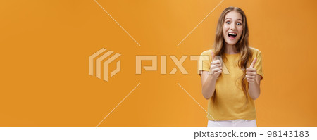 Excited girl expressed support and cheer raising thumbs up in approval and like gesture smiling optimistic and positive being amused with awesome idea standing pleased over orange background 98143183