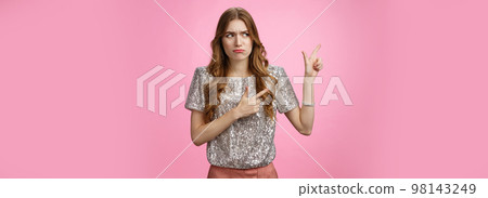 Displeased arrogant snobbish young rich glamour girl looking displeased cringe pointing left sideways, dislike place standing awkward insecure, expressing aversion reluctance, pink background 98143249