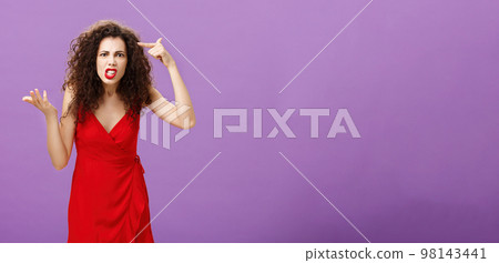 Outraged and pissed wife critisize dumb idea, outraged and fed up with stupid husband actions rolling finger near temple gesturing with raised palm, being angry and questioned over purple background Outraged and pissed wife critisize dumb idea, outraged and fed up with stupid husband actions rolling finger near temple gesturing with raised palm, being angry and questioned over purple background 98143441