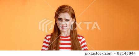 Cute disgusted redhead girl cringe from aversion bad awful smell, frowning grimace disappointed, clench teeth bothered, express dislike and reluctance, feel bad dissatisfied, refuse offer 98143944