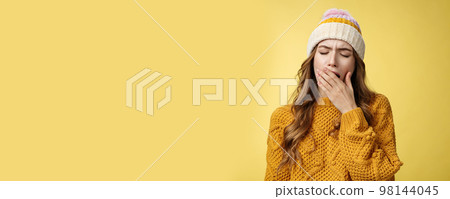 Close-up shot tired yawning cute exhausted european woman wearing hat sweater cover opened mouth feel sleepy drained wanna lay-down take nap, not morning person, yellow background Close-up shot tired yawning cute exhausted european woman wearing hat sweater cover opened mouth feel sleepy drained wanna lay-down take nap, not morning person, yellow background 98144045