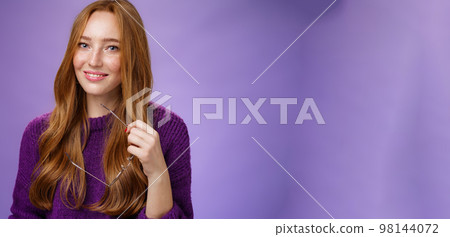 Close-up shot of charming tender and cute redhead woman in purple sweater holding glasses and smiling broadly as having nice friendly conversation against violet background Close-up shot of charming tender and cute redhead woman in purple sweater holding glasses and smiling broadly as having nice friendly conversation against violet background 98144072