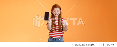 Impressed excited happy redhead woman smiling broadly, hold smartphone, pointing cellphone screen, thrilled amazed introduce fascinating application, stand orange background rejoice Impressed excited happy redhead woman smiling broadly, hold smartphone, pointing cellphone screen, thrilled amazed introduce fascinating application, stand orange background rejoice 98144076