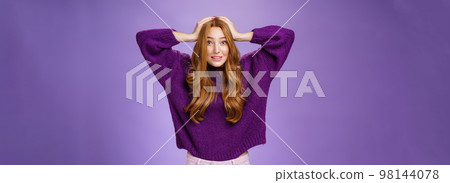 Cute european redhead 20s woman acting nervous, holding hands on head raising eyebrows in worry and anxiety, panicking being troubled think up plan posing over purple background 98144078