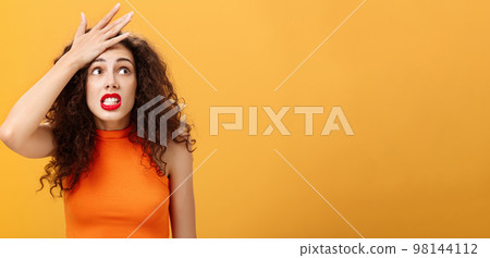 Shit I totally forgot about appointment. Nervous panicking displeased young european female with curly hair punching forehead with palm popping eyes anxiously at upper right corner making mistake 98144112