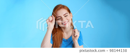 Close-up tender caring cute redhead 20s female tilt head, close eyes smiling dreamy, make winner dance, raise fist pumps celebration good news, stand optimistic good mood, blue background 98144138