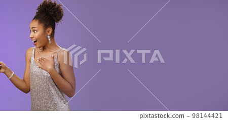 Impressed speechless thrilled elegant young african-american woman see celebrity press palm chest heartbeat fast pointing looking left amused astonished standing blue background amazed 98144421