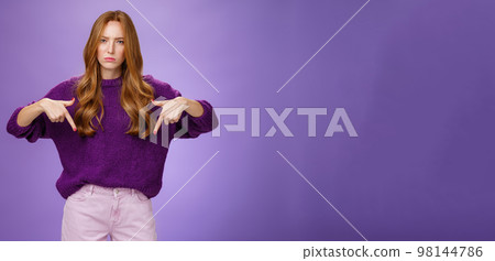 Woman dissatisfied with bad quality of service. Portrait of upset disappointed redhead female frowning and sulking as pointing down demanding explanations of bad product over violet wall 98144786