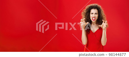 Woman like panter wanting scratch eyes of enemy. Portrait of pissed angry and pressured fed up woman clenching teeth and hands as if choking enemy with hate and anger in eyes being scary over red wall 98144877