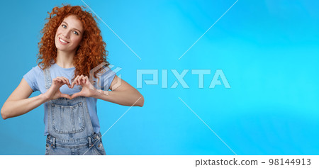 Caring tender lovely redhead girlfriend express sympathy tenderness gentle sympathy tilt head smiling broadly show heart love gesture chest cherish passionate romantic feelings, blue background 98144913