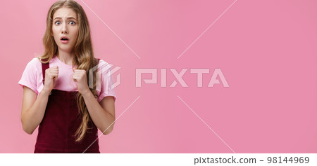 Young silly coward girl feeling insecure and scared stand up for herself raising clenched fists pressed to chest in self-defense open mouth in shock and fear looking scared at camera, being bullied 98144969