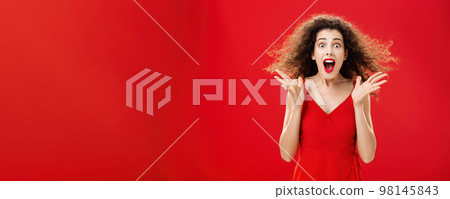 Portrait of surprised and astonished speechless curly-haired woman in red luxurious dress dropping jaw from amazement popping eyes at camera and gesturing emotive and shocked over background Portrait of surprised and astonished speechless curly-haired woman in red luxurious dress dropping jaw from amazement popping eyes at camera and gesturing emotive and shocked over background 98145843