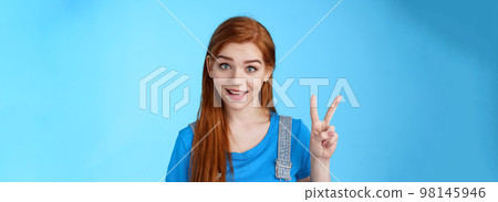 Cheerful attractive redhead caucasian girl smiling joyfully talking, order two peaces, show second number, peace victory sign, stand carefree, upbeat emotions, stand blue background Cheerful attractive redhead caucasian girl smiling joyfully talking, order two peaces, show second number, peace victory sign, stand carefree, upbeat emotions, stand blue background 98145946